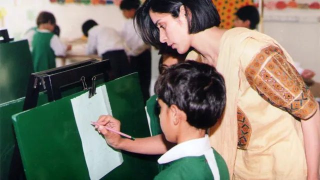 A teacher leans over to help a boy painting at an easel