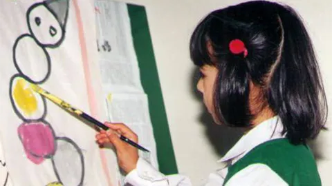 A pupil paints during an art lesson at Pearl Valley Public School A girl with a red hair clip painting a colourful picture