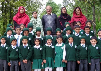Young pupils in green uniforms and caps with adults standing behind them under trees