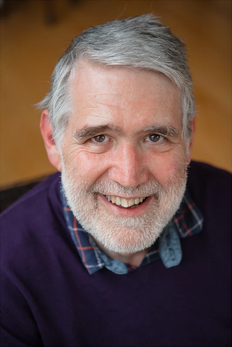 Portrait of a smiling grey-haired, bearded man in a purple jumper and checked shirt