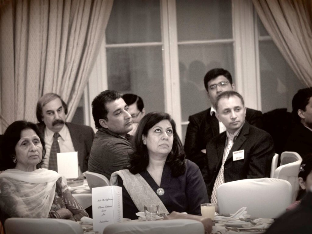Sepia photo of seated guests listening, with a Please Support Quest for Education table card