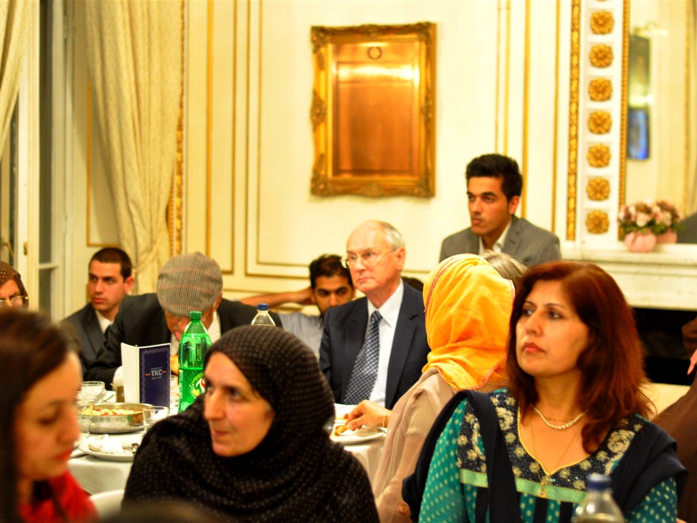 Guests seated around dinner tables in an ornate room, several women in traditional dress