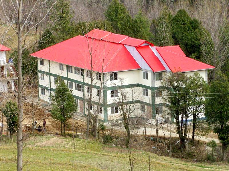 A white three-storey school building with a red roof on a wooded hillside