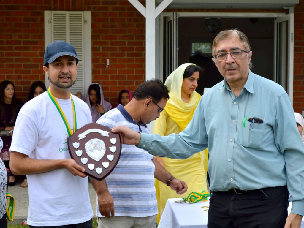 A cricketer in a Quest for Education t-shirt being presented with a shield trophy