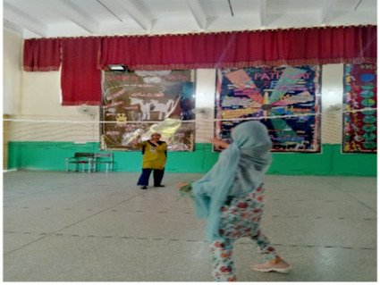 Two players in a badminton rally in a hall with a red stage curtain