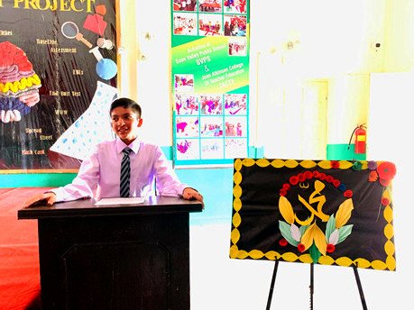 A boy in school uniform speaking from a lectern beside a decorated calligraphy board