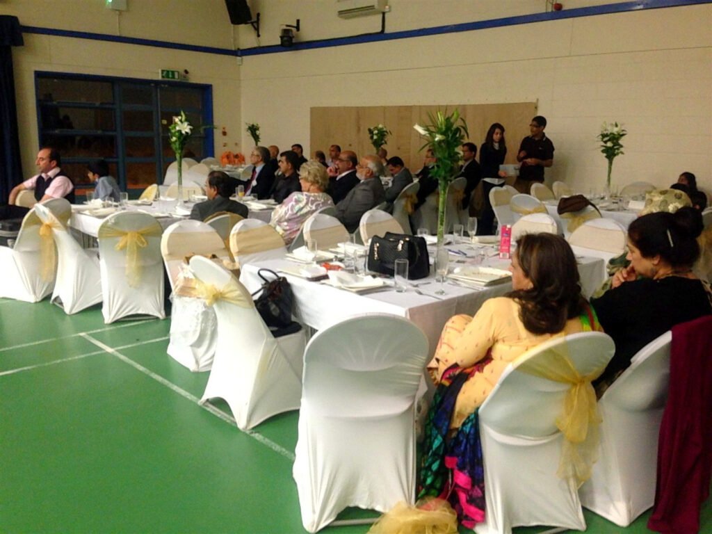 Guests at white-dressed tables with lily centrepieces in a community hall