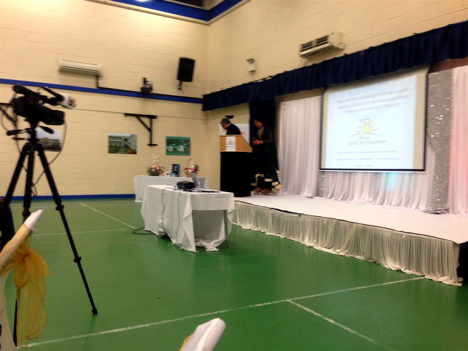 Stage with lectern, projected Quest for Education slide and video camera in a hall.