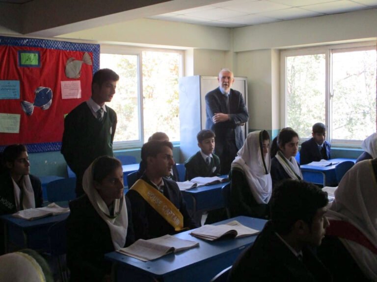 Older girls and boys in school uniform in a classroom with a visitor