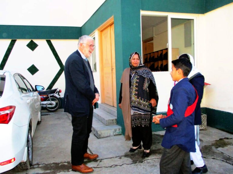 Staff and a pupil prefect welcome a visitor outside a school building