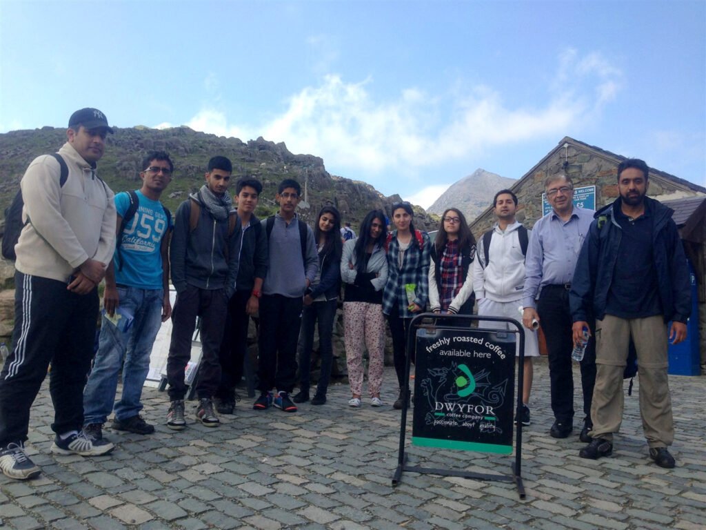 Group of walkers posing at a mountain trailhead beside a stone building
