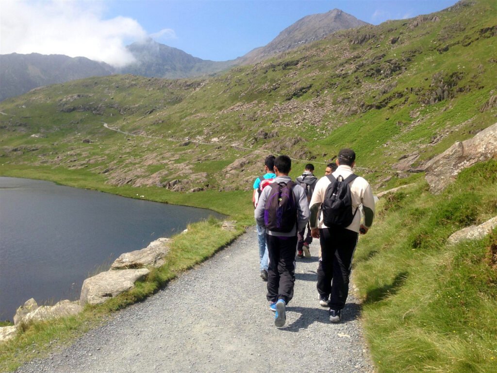 Walkers from behind on a lakeside path heading towards a mountain peak