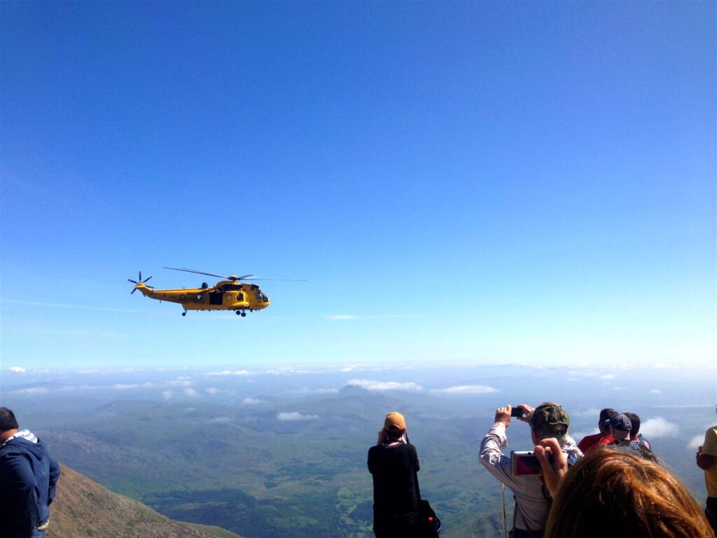 Yellow helicopter flying past walkers at the mountain summit