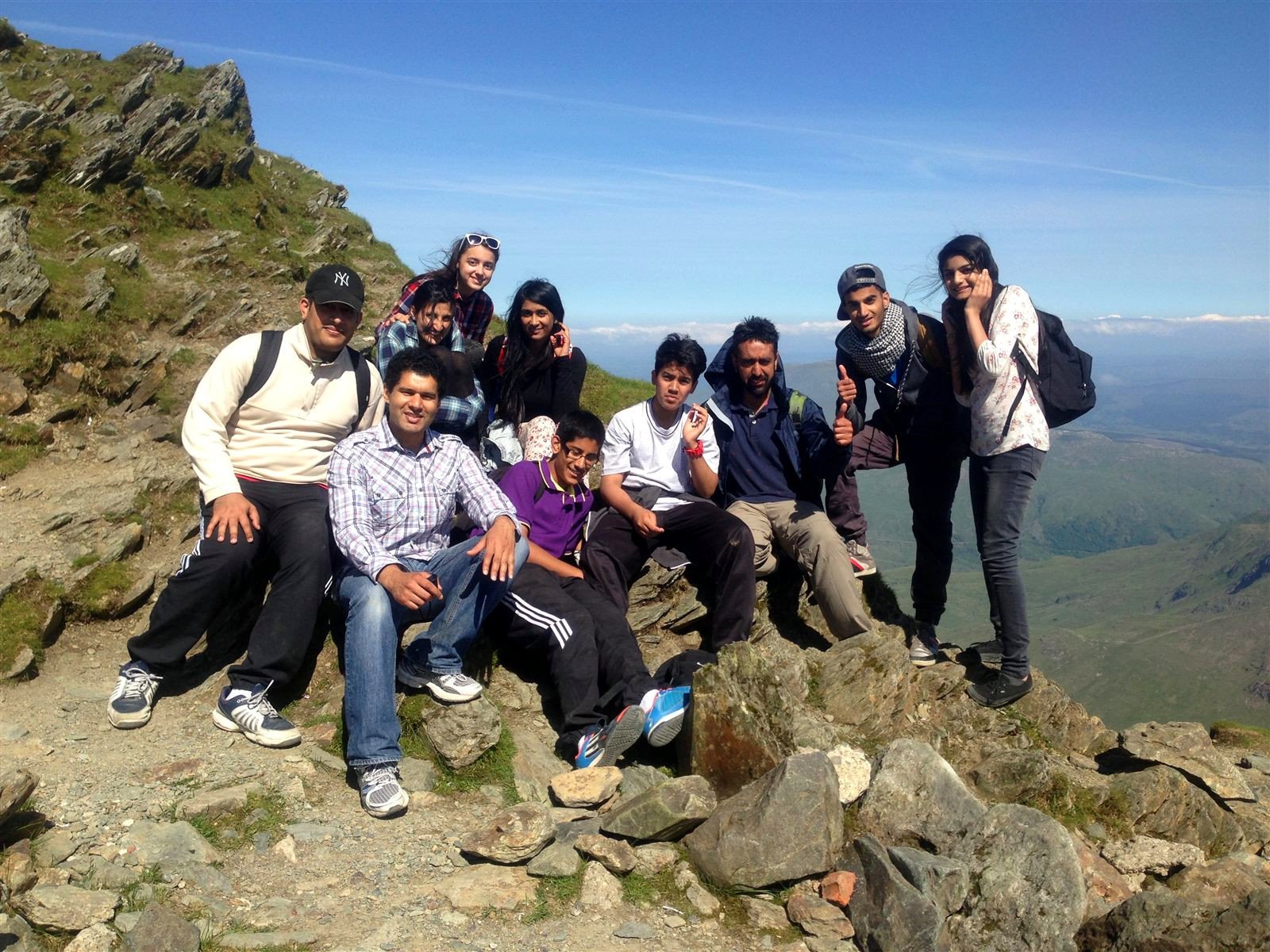 Group of smiling walkers posing on rocks near the summit under blue sky