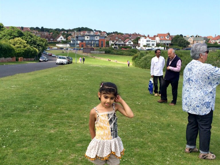 Young girl on a grassy slope with adult walkers behind on a sunny day