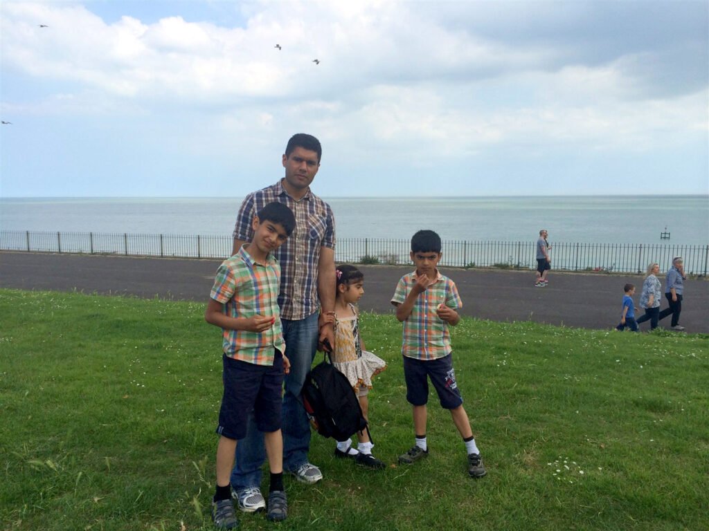 Mobeen Anwar and three children posing on grass in front of the sea